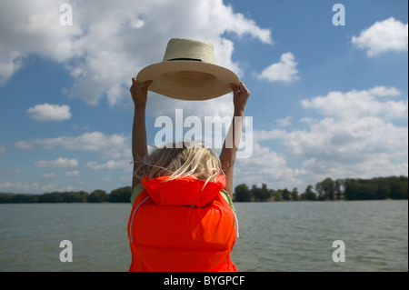 Ragazza di indossare il giubbotto di salvataggio, tenendo hat dal lago Foto Stock