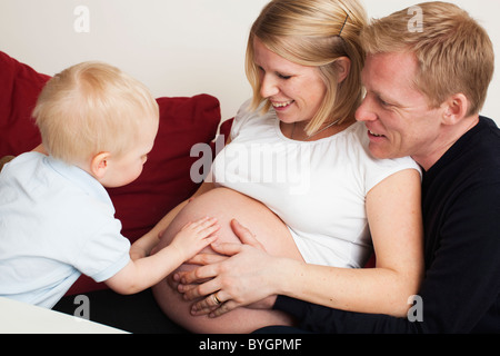 Famiglia di toccare le donne incinte stomaco sul divano Foto Stock