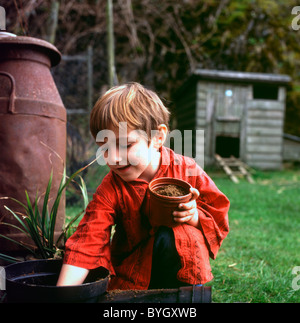 Un ragazzo giovane giardiniere accovacciato riempimento vasetti di plastica con il terreno per preparare per la semina di semi in primavera Wales UK KATHY DEWITT Foto Stock