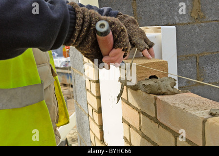 Chiusura del muratore le mani applicare mortaio su un Brickwall. Foto Stock