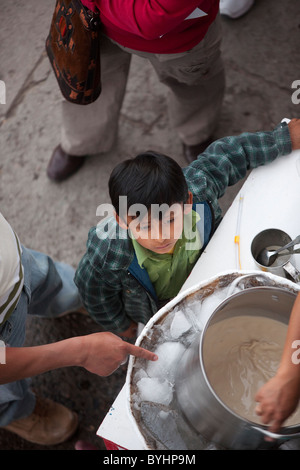 Un giovane ragazzo guarda una pentola di gelato venga venduto ad un weekend di fiera nella piazza principale di Ayacucho, Perù. Foto Stock