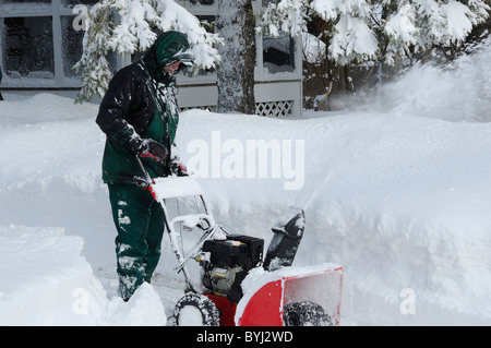 Uomo che utilizza un moderno lo spalaneve per cancellare un vialetto la mattina dopo un inverno di blizzard Foto Stock