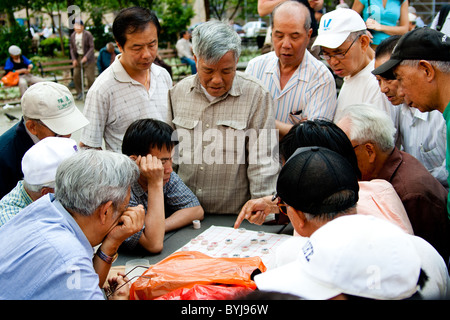 Asian i giocatori che giocano un consiglio strategico come gioco di scacchi cinesi, chiamato Xiangqi in Columbus Park, China Town, New York. Foto Stock