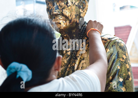 Donna mettendo la carta oro su una figura religiosa, Wat Mahannapharam Worawiharn, Bangkok, Thailandia Foto Stock