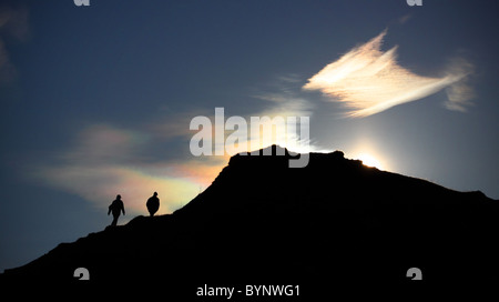 Stagliano giovane camminare su per una collina contro un cielo blu con sun vistosa dietro di loro Foto Stock