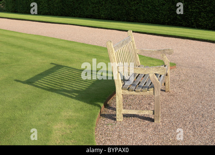 Vuoto vacante in una panchina nel parco di fronte al sole su un sentiero di ghiaia attraverso un parco con ordinatamente erba falciata prati con lunga ombra nel Regno Unito Foto Stock