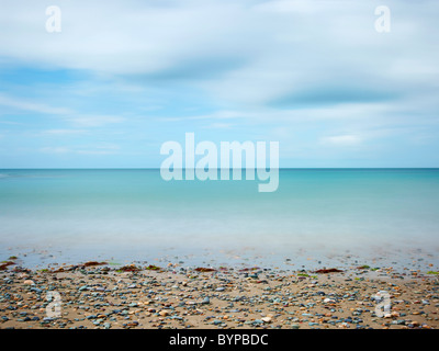 Seascape fotografia della chiesa bay Anglesey nel Galles, una lunga esposizione alla luce del giorno dando il movimento nel cielo e mare con spiaggia ghiaiosa Foto Stock