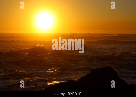 Brillante arancio profondo di close-up di un oceano al tramonto con onde instabile la spruzzatura di acqua nell'aria. Seal Rock, Oregon, Stati Uniti d'America. Foto Stock