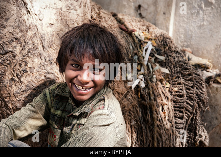 Felice giovani poveri di casta inferiore Indian street boy sorridente appoggiato contro un albero. Andhra Pradesh, India Foto Stock