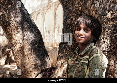 Felice giovani poveri di casta inferiore Indian street boy sorridente appoggiato contro un albero. Andhra Pradesh, India Foto Stock