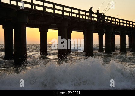 Swakopmund, Namibia, silhouette di pescatori sul molo al tramonto, le onde che si infrangono in primo piano, Namibia Foto Stock