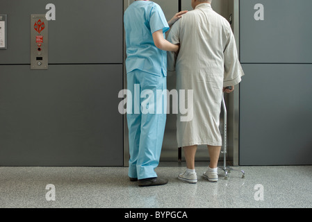 L'infermiera aiutando paziente attesa per ascensore nel corridoio dell'ospedale Foto Stock