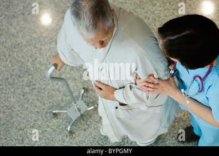 L'infermiera aiutando paziente senior a piedi nel corridoio Foto Stock