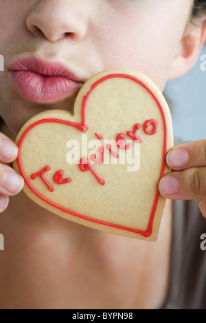 Donna raggrinzamenti labbra, tenendo a forma di cuore cookie Foto Stock