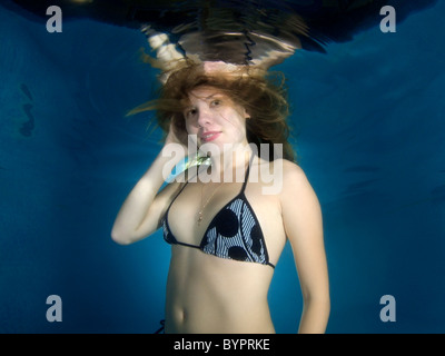 Una giovane donna con grandi capelli in posa di un subacqueo in piscina Foto Stock