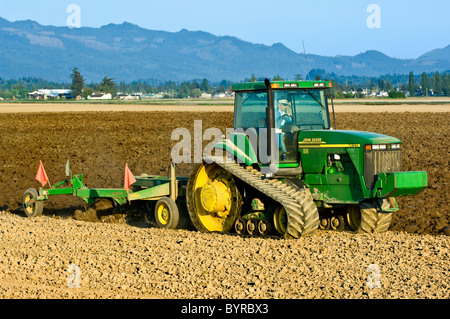 Un John Deere trattore cingolato tirando un aratro reversibile si prepara un campo per la semina delle patate / vicino a Burlington, Washington, Stati Uniti d'America Foto Stock