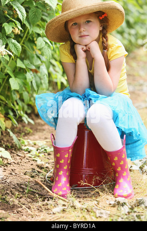 Una ragazza che indossa un cappello di paglia e seduta su un grande secchio rosso; troutdale, Oregon, Stati Uniti d'America Foto Stock