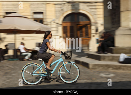 Il panning immagine di una giovane donna di cavalcare la sua bicicletta in una città tradizionale piazza. Foto Stock