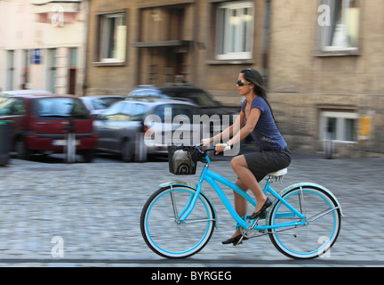 Il panning immagine di una giovane donna di cavalcare la sua bicicletta in una città tradizionale piazza. Foto Stock