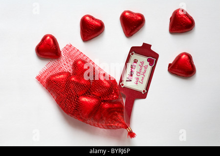 Valentino di cioccolato al latte di cuori avvolti nel foglio in plastica rosso fuoriuscita dal sacchetto reticolare isolati su sfondo bianco - regalo ideale per il giorno di San Valentino Foto Stock