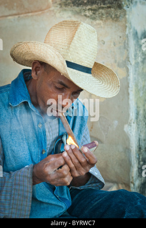 Giovane con cappello di paglia illuminazione di un sigaro, Trinidad, Sancti Spiritus, Cuba, Caraibi Foto Stock