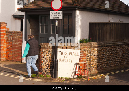 Una donna cammina davanti ad una lettura del segno parete non sicuri nel Regno Unito Foto Stock