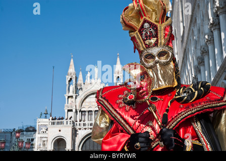 Maschera Veneziana durante il carnevale con rosso, nero e oro travestimento, posa con la basilica di San Marco in background Foto Stock