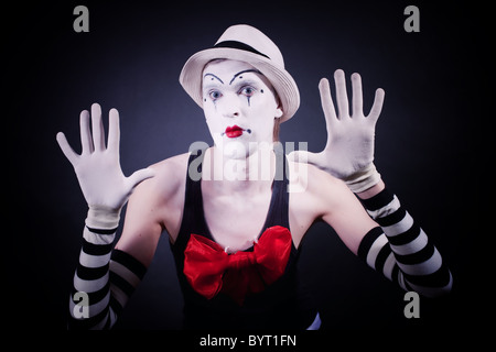 Mime con fiocco rosso in un cappello bianco e guanti a strisce su sfondo nero Foto Stock