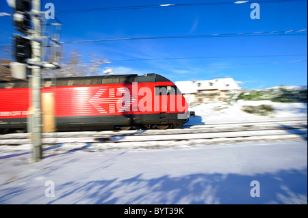 Un treno svizzero accelerando attraverso un paesaggio innevato a metà inverno. Motion Blur utilizzato per dare il senso della velocità. Foto Stock