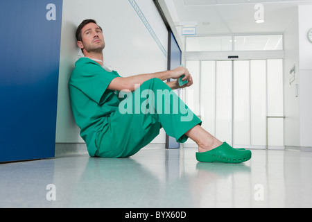 Dottore in scrubs, appoggiato sul pavimento Foto Stock