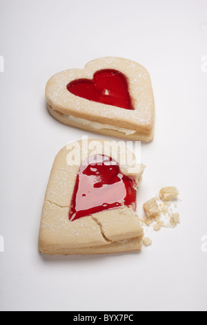 Fotografia di cuore i biscotti di forma riempita con marmellata di rosso su sfondo bianco. Include rotto e biscotti sbriciolati. Il giorno di San Valentino del concetto. Foto Stock