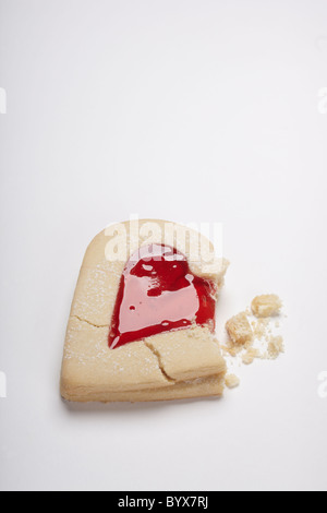 Fotografia di cuore i biscotti di forma riempita con marmellata di rosso su sfondo bianco. Include rotto e biscotti sbriciolati. Il giorno di San Valentino del concetto. Foto Stock