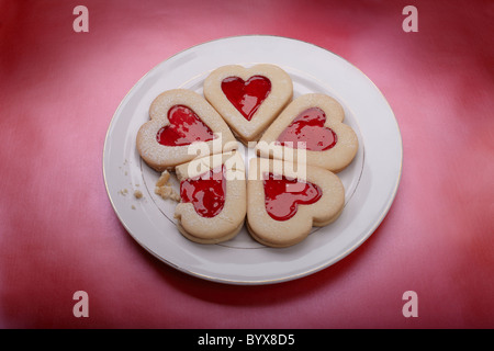 5 a forma di cuore i biscotti su una piastra bianca con sfondo rosso, un biscotto rotto Foto Stock