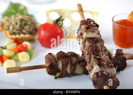 Gli spiedini di carne su un piatto di portata con pomodoro e verdure Foto Stock