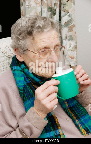 Donna anziana usando un inalatore di vapore inalazione di un decongestionante per raffreddori e bronchiti Foto Stock