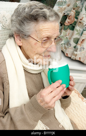 Donna anziana usando un inalatore di vapore inalazione di un decongestionante per raffreddori e bronchiti Foto Stock