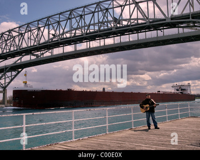 Freighter rende il modo sotto l'acqua blu ponte collega Port Huron Michigan & Sarnia Ontario uomo suona la chitarra sul Boardwalk Foto Stock