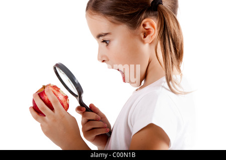 Bambina con una lente di ingrandimento di ispezionare i microbi su una mela rossa Foto Stock