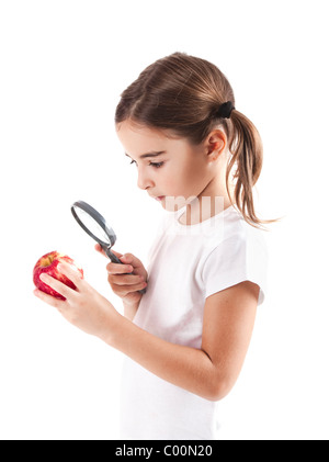 Bambina con una lente di ingrandimento di ispezionare i microbi su una mela rossa Foto Stock