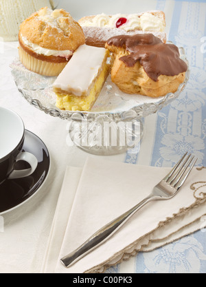 Il tè del pomeriggio con selezione di torte di panna sulla torta di vetro stand, Foto Stock