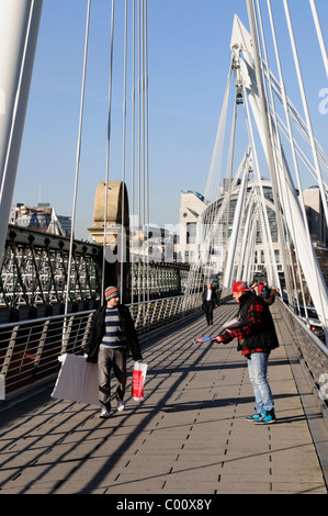 Un grande problema venditore in Hungerford ponte pedonale, con la stazione di Charing Cross in background, London, England, Regno Unito Foto Stock