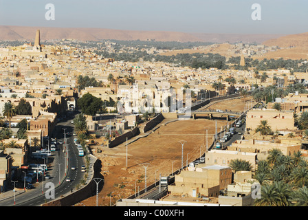 Algeria, Ghardaia, vista città con i veicoli su strada di mattoni di fango e di abitazione minareto alto contro il cielo chiaro Foto Stock