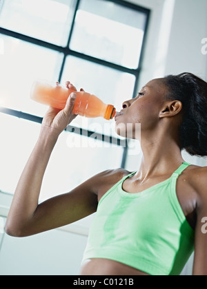 Giovane africano donna americana in sportswear con energy drink in palestra. Forma verticale, vita, spazio di copia Foto Stock