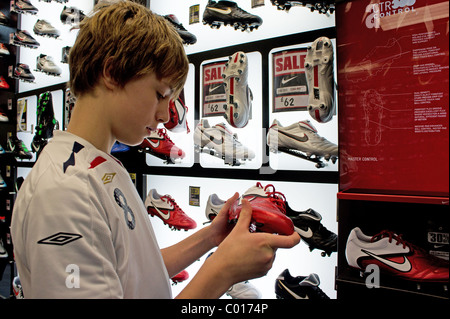 Un ragazzo adolescente guardando gli scarpini da calcio in una sporting goods shop, Regno Unito Foto Stock