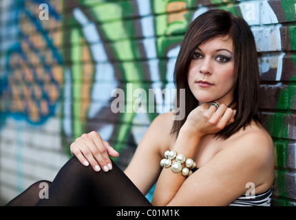 Ritratto di una giovane donna con i capelli scuri, che pongono di fronte a un muro con graffiti Foto Stock