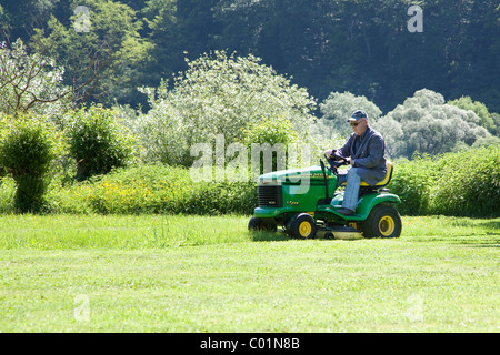 Uomo anziano Falciare il prato su un John Deere a sedersi sul tosaerba, Bengel, Renania-Palatinato, Germania, Europa Foto Stock