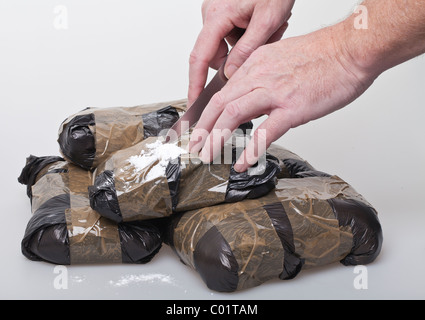 Pacchetti di polvere bianca (farmaci) avvolto in plastica nera essendo aperta tagliata con un coltello Foto Stock