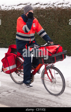 Un Royal Mail portalettere che mostra il movimento in bicicletta sul suo giro nella neve nel Regno Unito Foto Stock