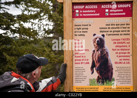 Uomo che guarda un orso segno di avvertimento sul sentiero di consolazione lago vicino al Lago Moraine il Parco Nazionale di Banff Alberta, Canada Foto Stock