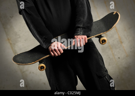 La sezione centrale dell'uomo azienda skateboard su sfondo di calcestruzzo con spotlight Foto Stock